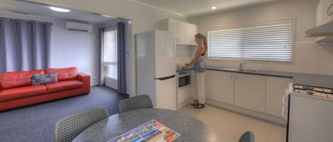 Un espacio habitable compacto con kitchenette, zona de comedor y sofá rojo.
