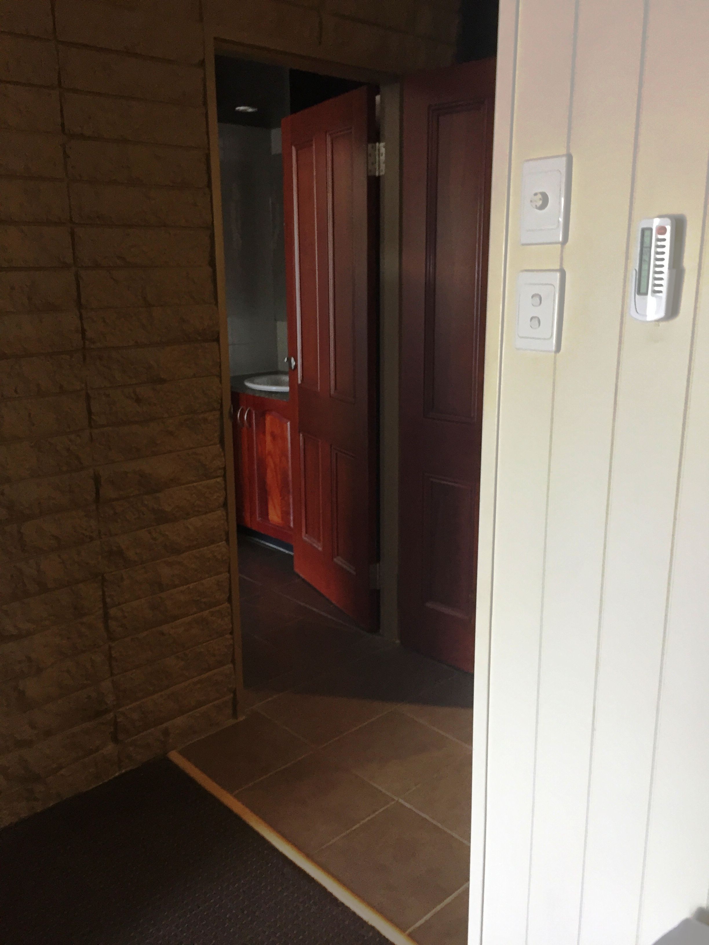 Un corridoio con una porta in legno, un interruttore della luce e un termostato sulla parete.