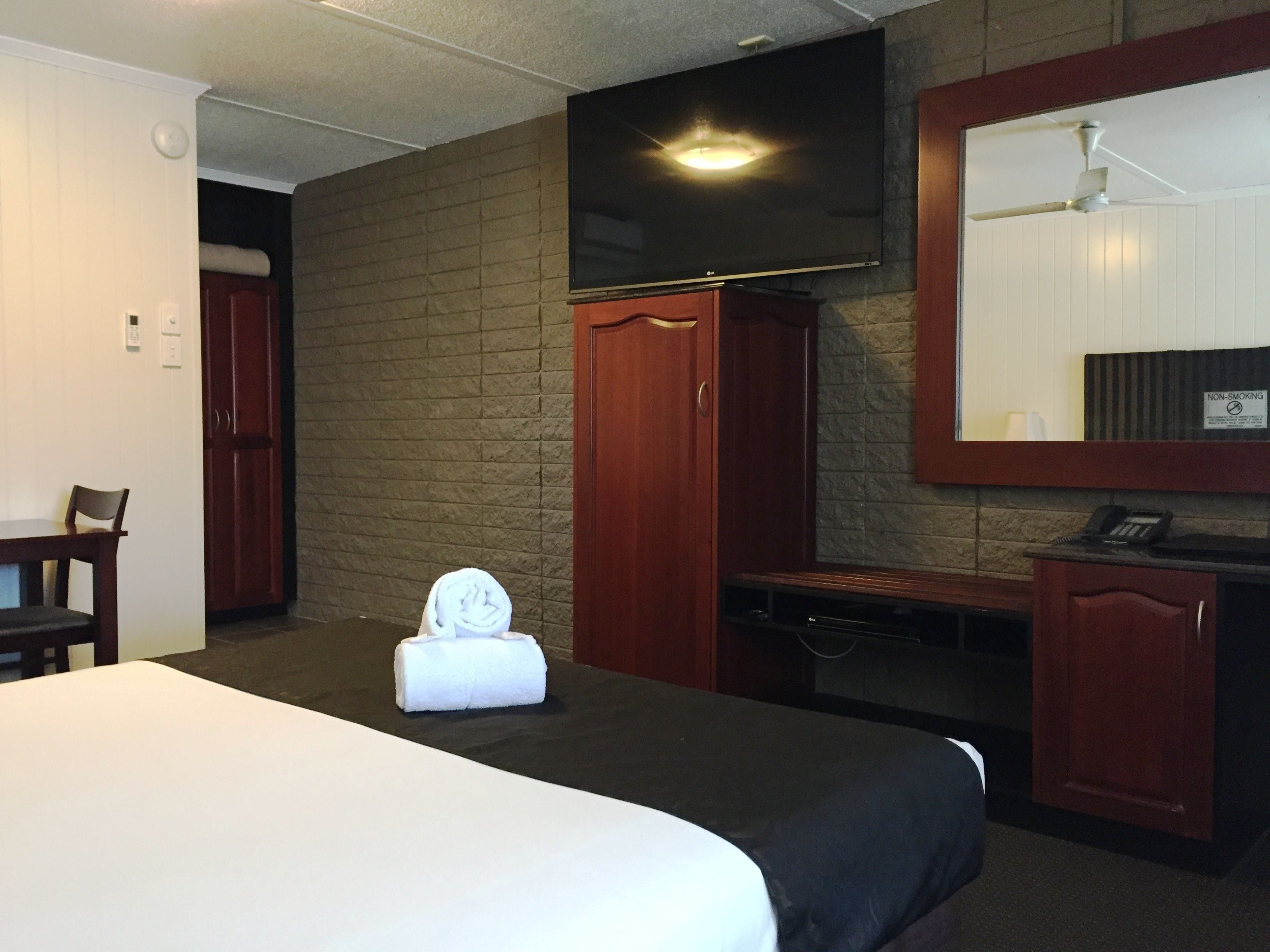 Quarto de hotel com cama, escrivaninha, cadeira, espelho, telefone e placa indicando que não é área para fumantes.