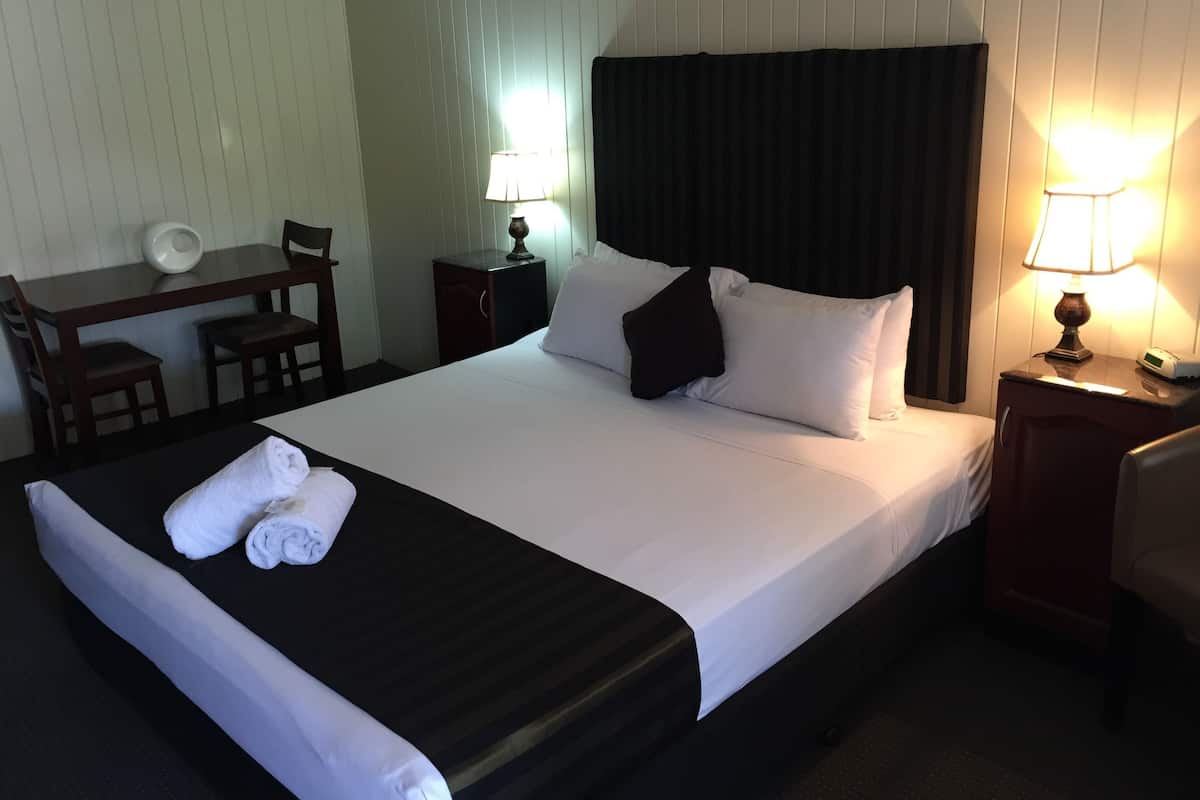 A neatly made bed with white linens and a black headboard, a desk with a chair, and two bedside lamps.