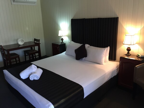A neatly made bed with white linens and a black headboard, a desk with a chair, and two bedside lamps.
