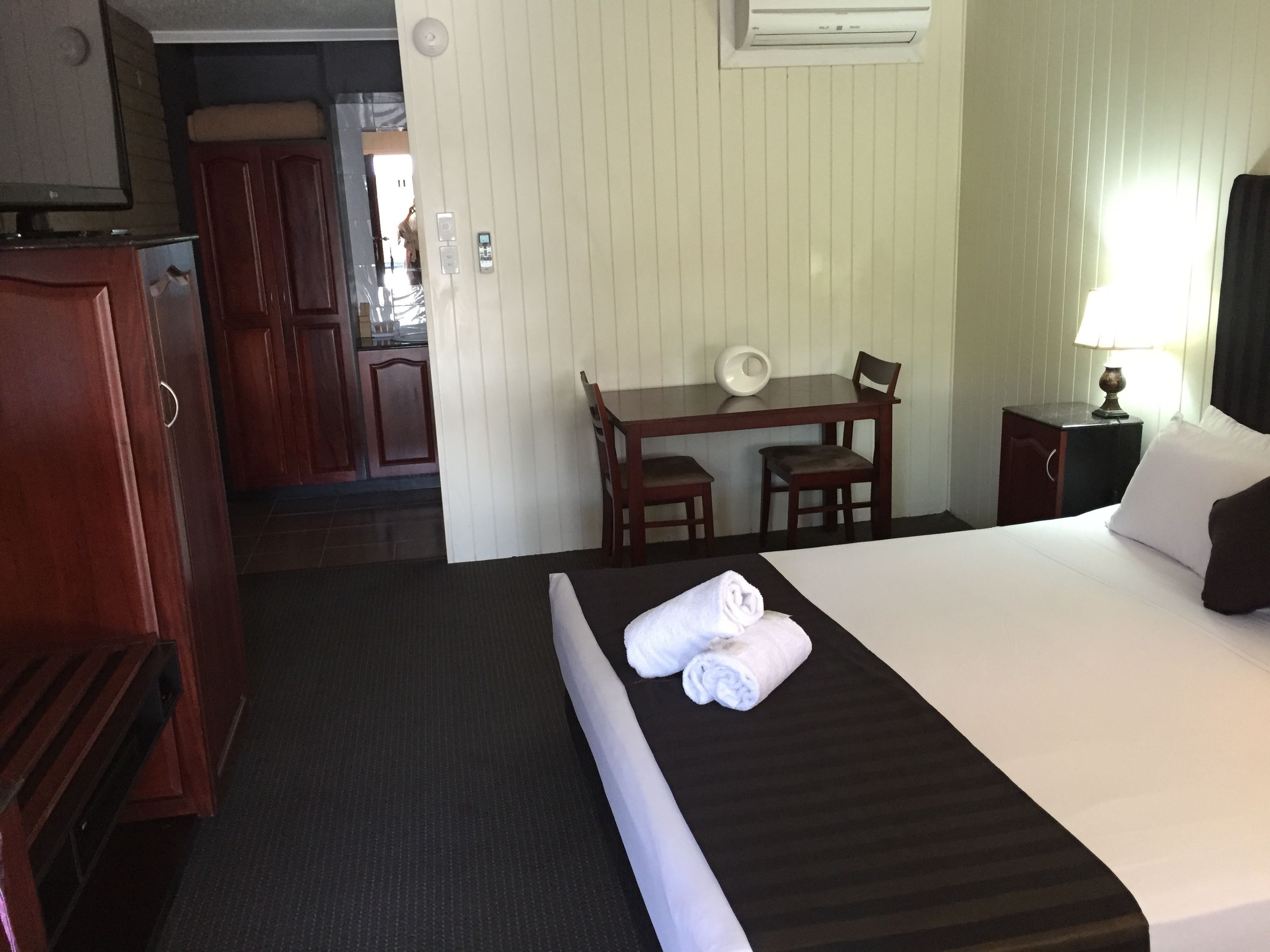 A hotel room with a bed, a desk, a chair, a nightstand, and a wardrobe.