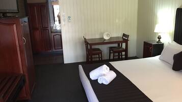 A hotel room with a bed, a desk, a chair, a nightstand, and a wardrobe.
