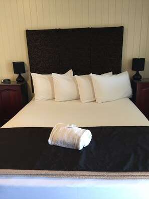 A neatly made bed with white bedding and a rolled towel, two bedside tables with lamps, and a dark headboard. - Country Plaza Motor Inn (West Mackay)