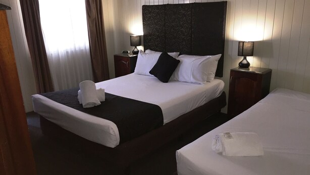 A hotel room with a large bed, two bedside tables, a nightstand, and a window with curtains. - Country Plaza Motor Inn (West Mackay)