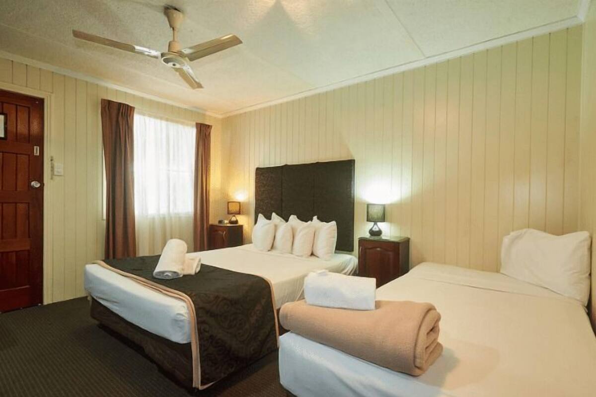 A hotel room with two beds, a ceiling fan, and a window with curtains.