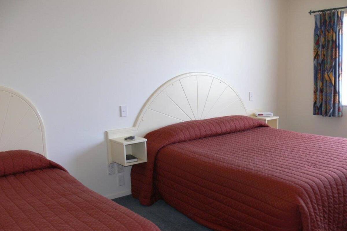 A room with two beds, each with a white headboard and a bedside table.