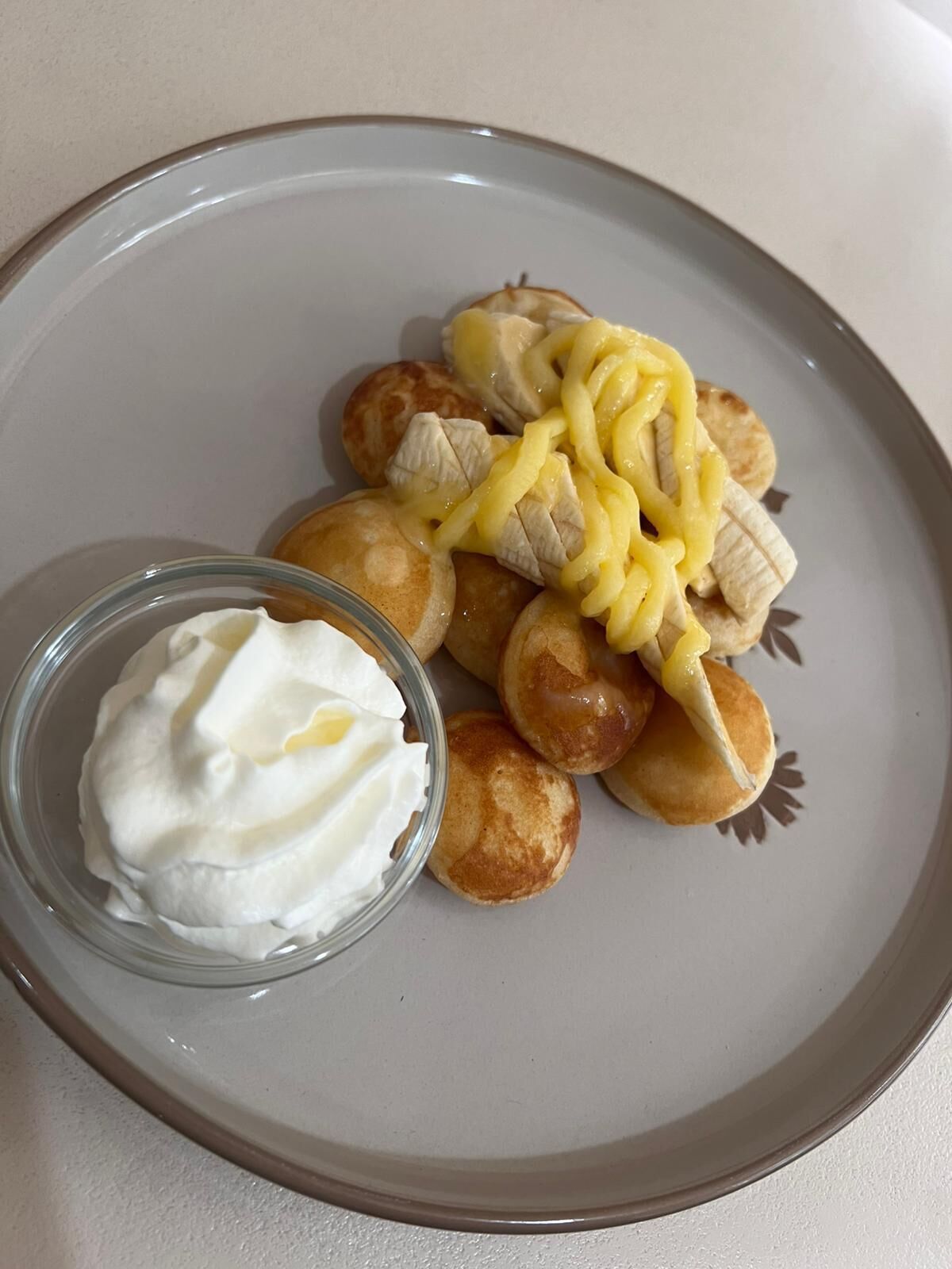 Un piatto con pancake, fettine di banana e una piccola ciotola di panna acida.