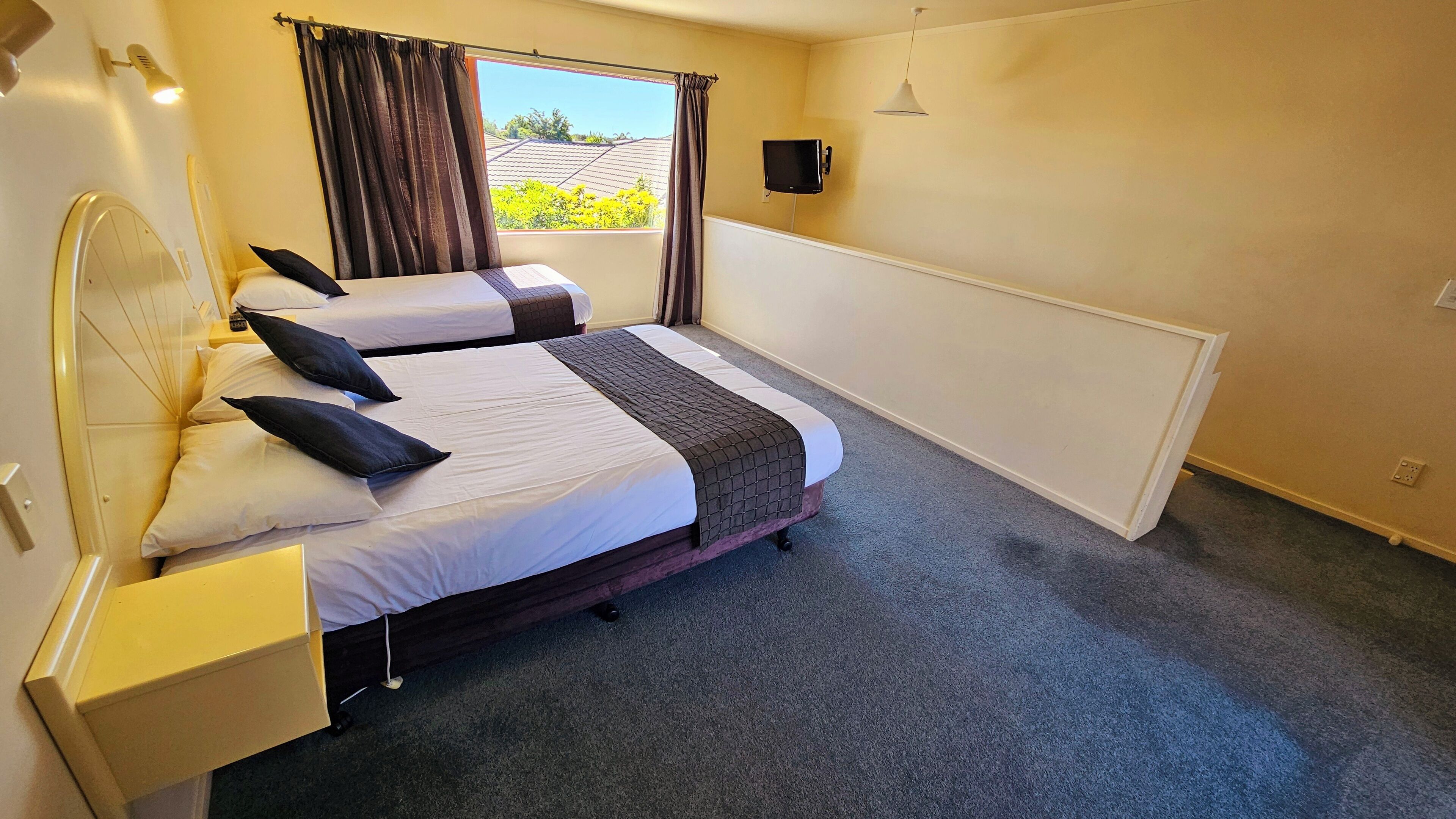 Habitación de hotel con dos camas, una ventana con cortinas, un televisor de pantalla plana y una lámpara de noche.