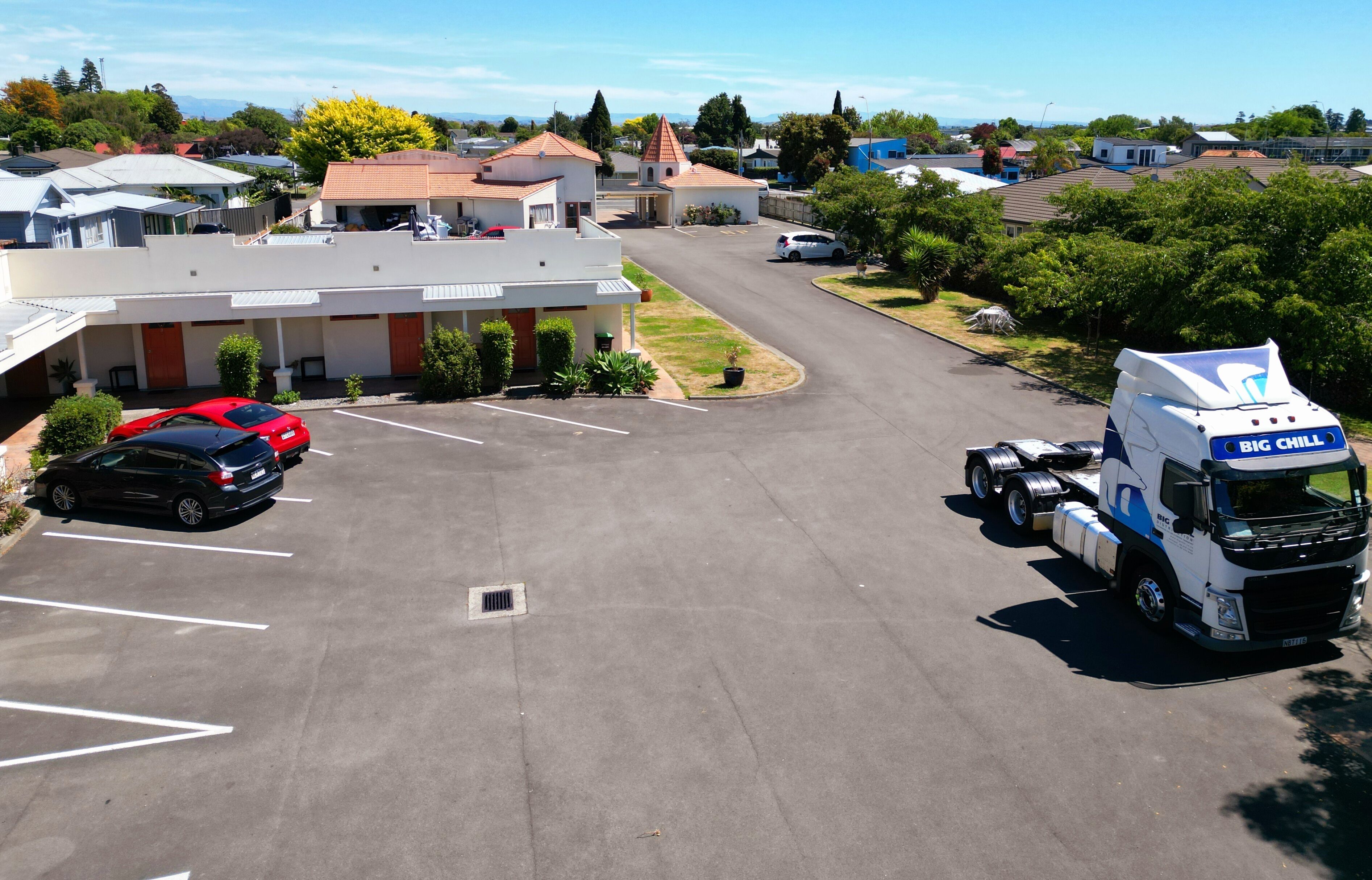 Un parking avec un bâtiment blanc, une voiture rouge et un camion blanc sur lequel on peut lire « BIG CHILL » sur le côté.
