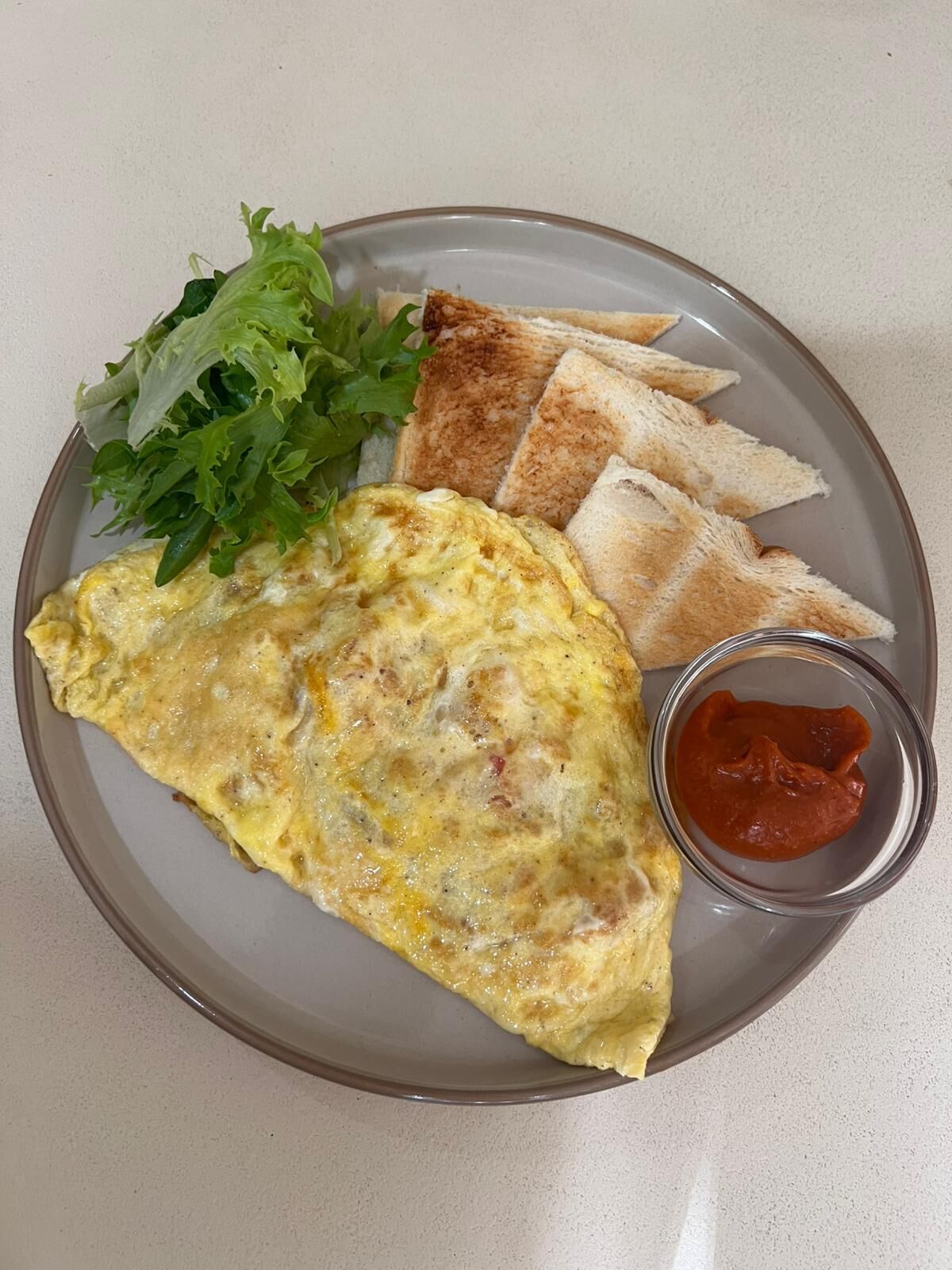 Une assiette avec une omelette, des tranches de pain grillé, de la laitue et un petit bol de sauce.