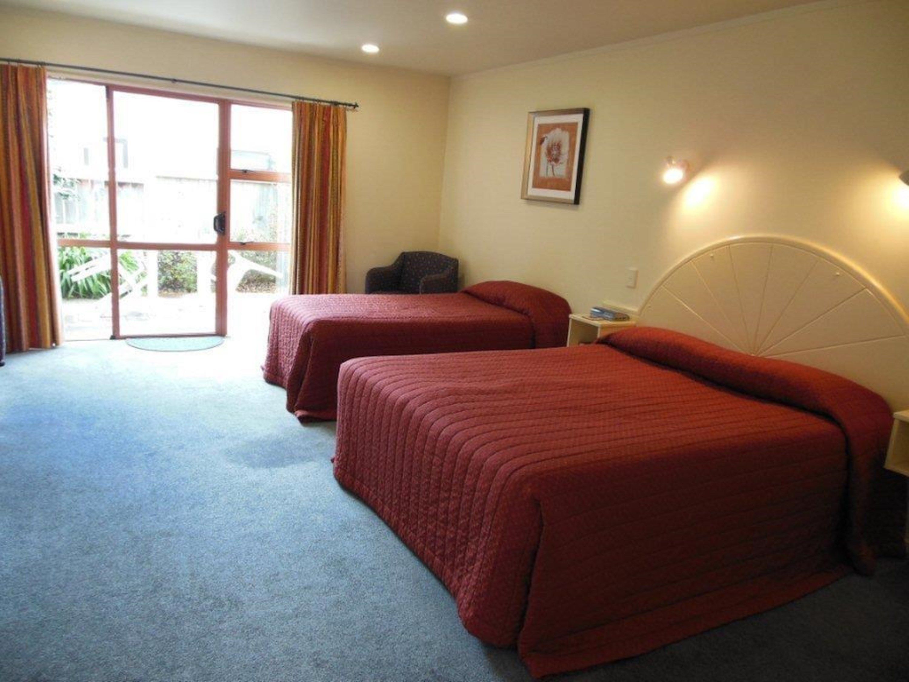 A hotel room with two beds, a chair, a desk, and a window with curtains.