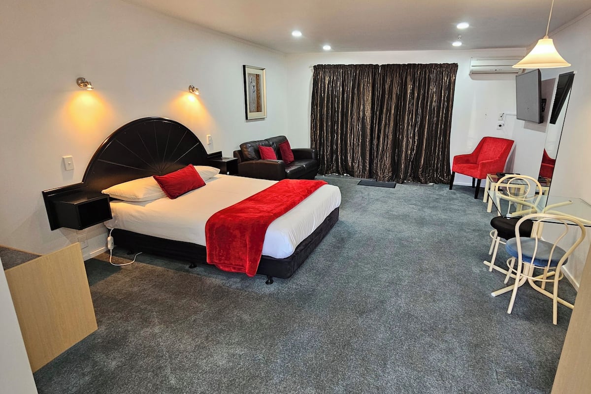 A hotel room with a large bed, a desk, a chair, and a television.