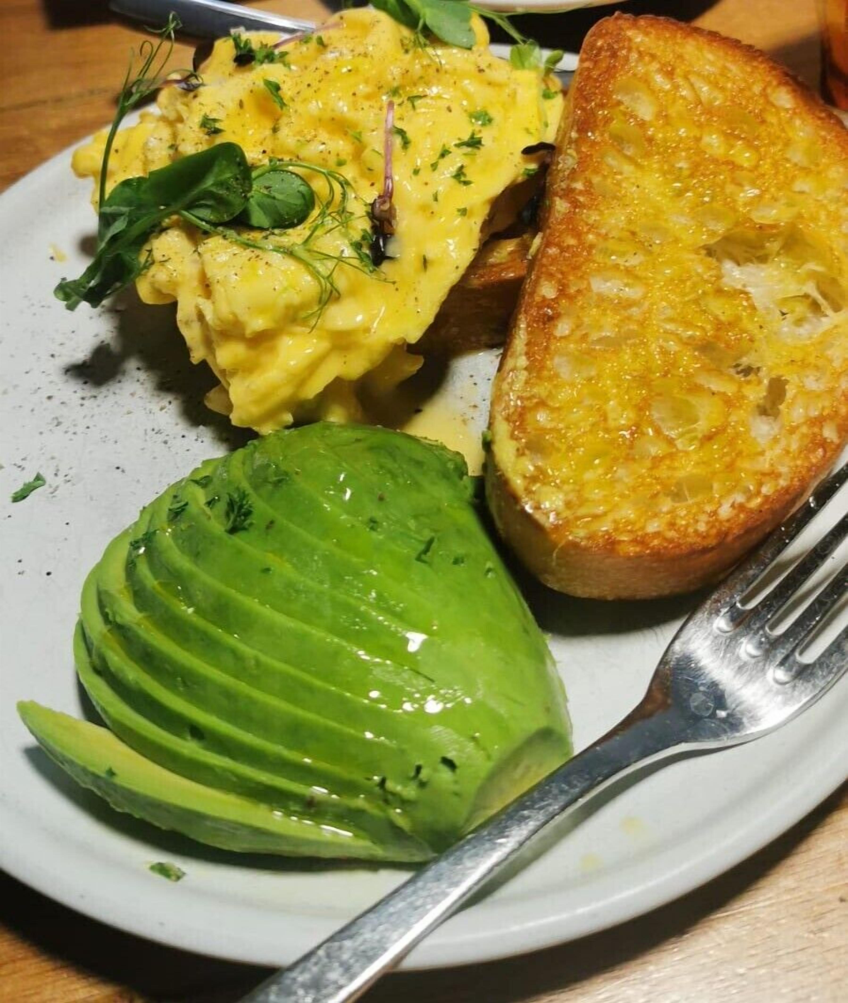 A plate with scrambled eggs, avocado, and toasted bread.