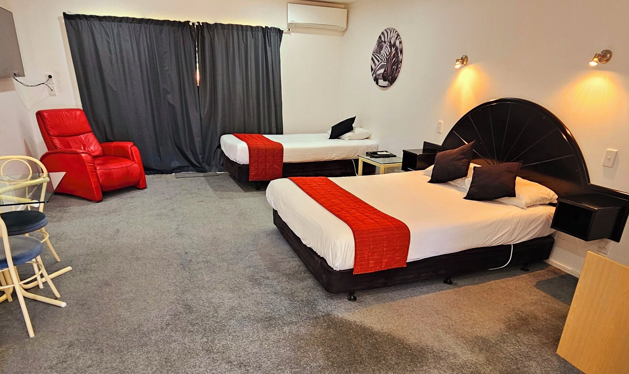 A hotel room with two beds, a red chair, a desk, and a large window with curtains.
