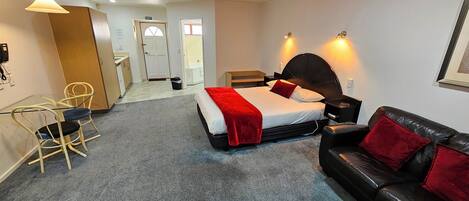 A hotel room with a bed, a black leather sofa, a desk with a chair, and a small table with a lamp.