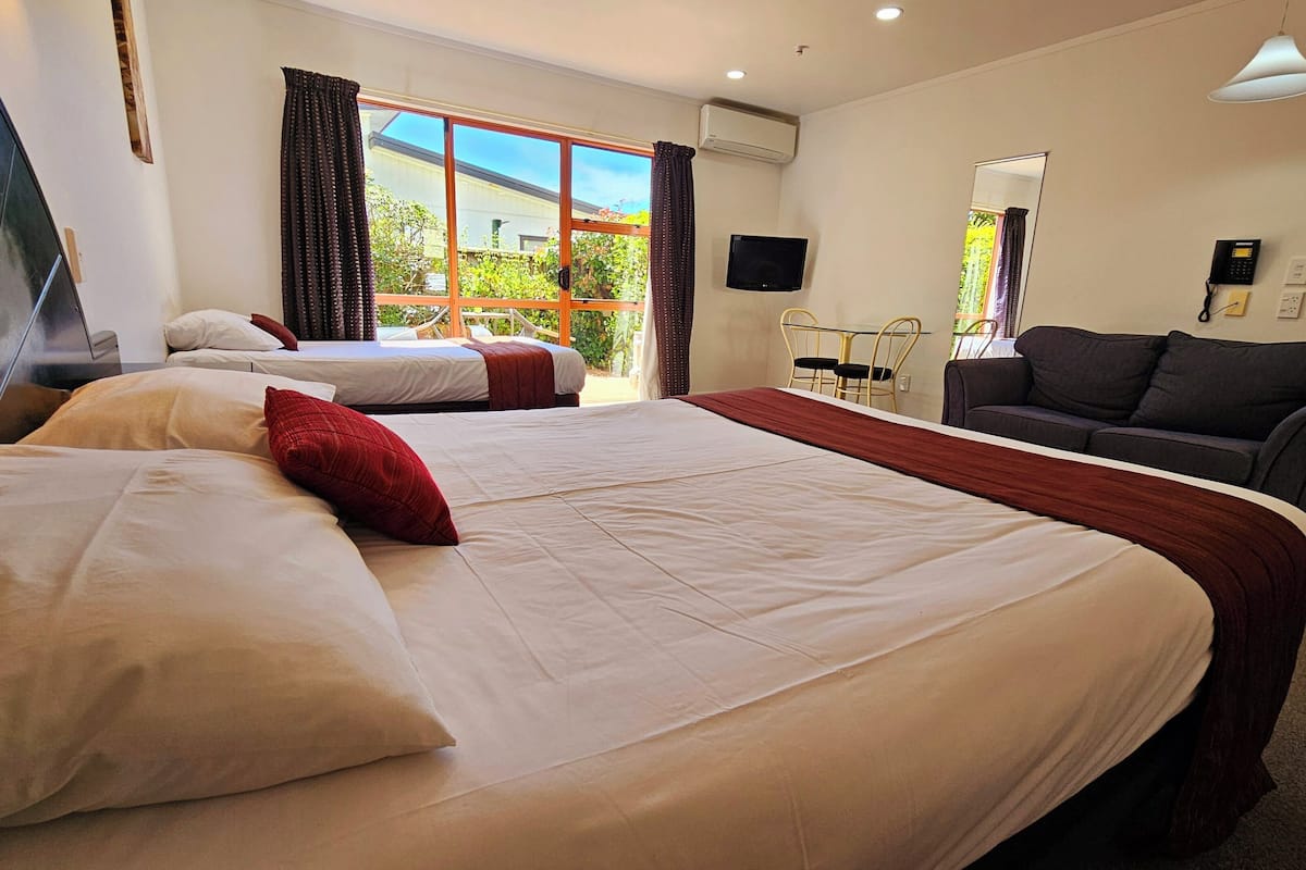 A hotel room with two beds, a sofa, a TV, and a window with curtains.