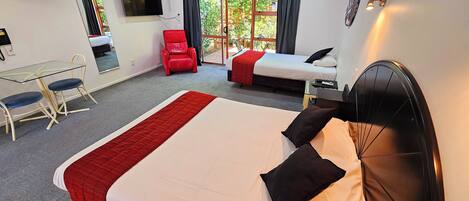 Habitación de hotel con una cama grande, un escritorio con una silla, una silla roja, un televisor y una ventana con cortinas.