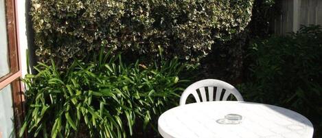 A round white table with chairs, a white fence, and a hedge in a garden area.