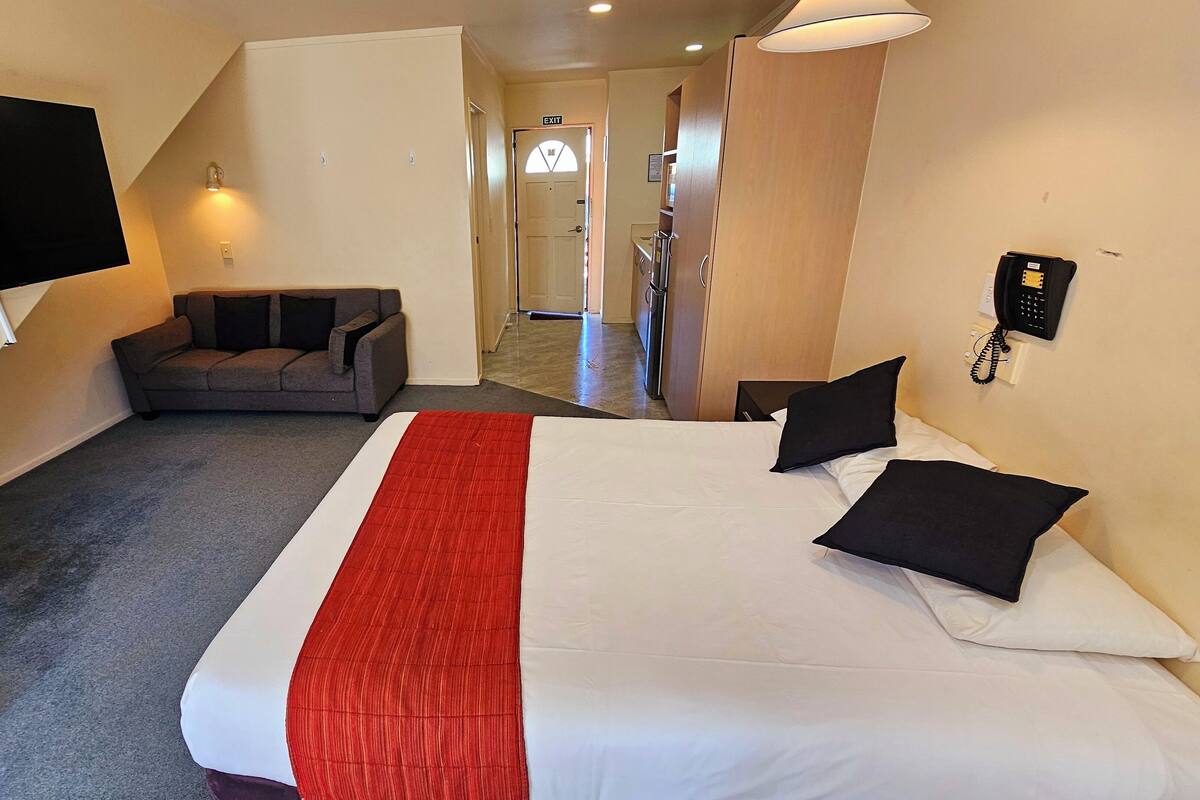 A hotel room with a bed, a TV mounted on the wall, a sofa, a telephone, and an exit sign.