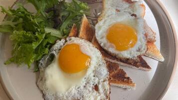 Un plato con dos huevos fritos sobre tostada, una ensalada y un recipiente pequeño con salsa.
