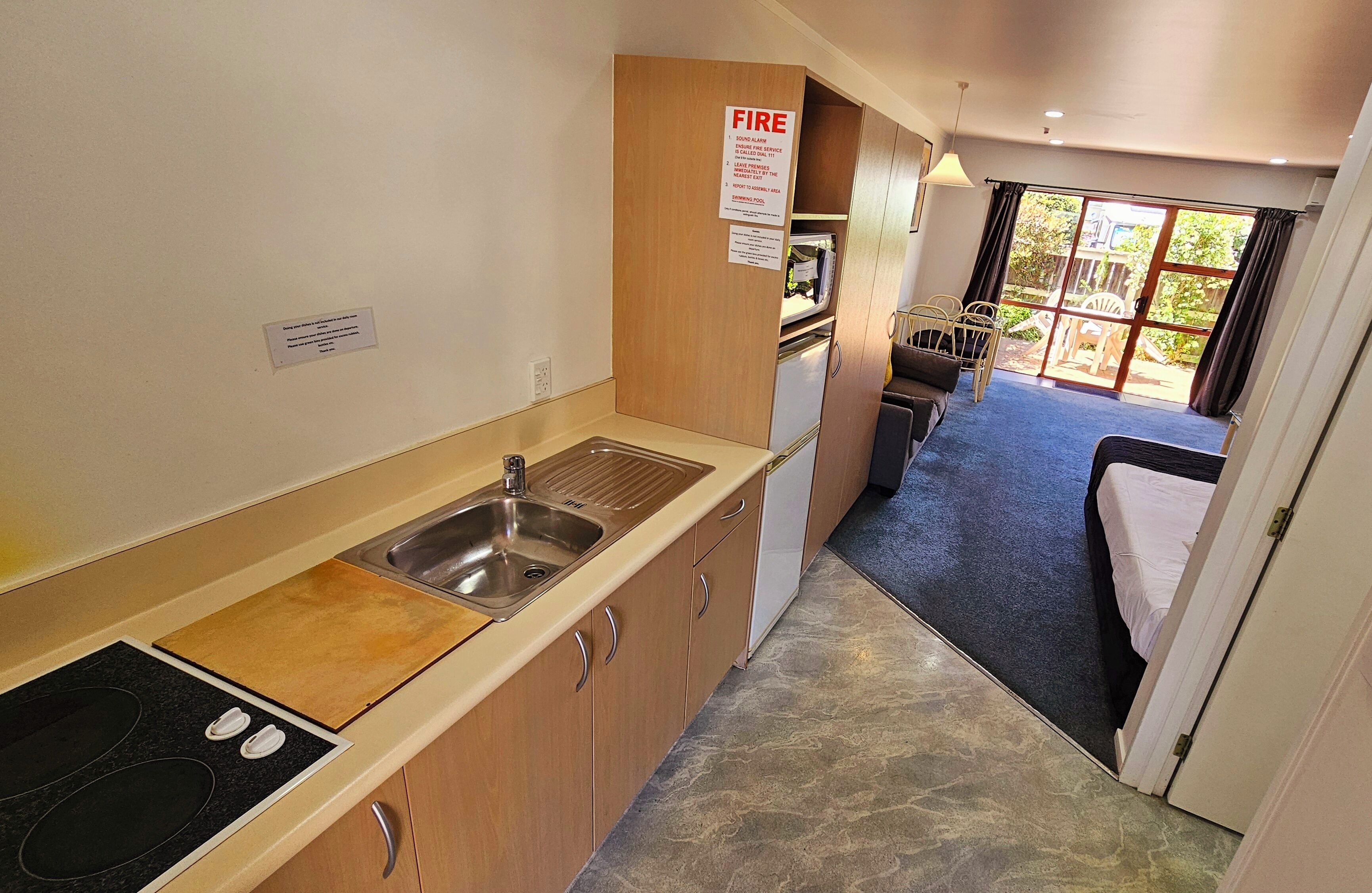 Une cuisine compacte équipée d’un évier, d’une cuisinière et de placards, qui donne sur une chambre avec un lit et une vue sur l’extérieur.