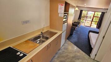 A compact kitchen with a sink, stove, and cabinets, leading to a bedroom with a bed and a view of the outdoors.