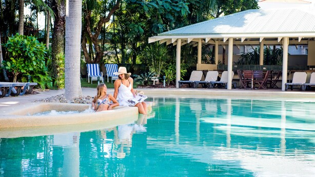 Un área de piscina con sillones de descanso y una zona de estar cubierta.