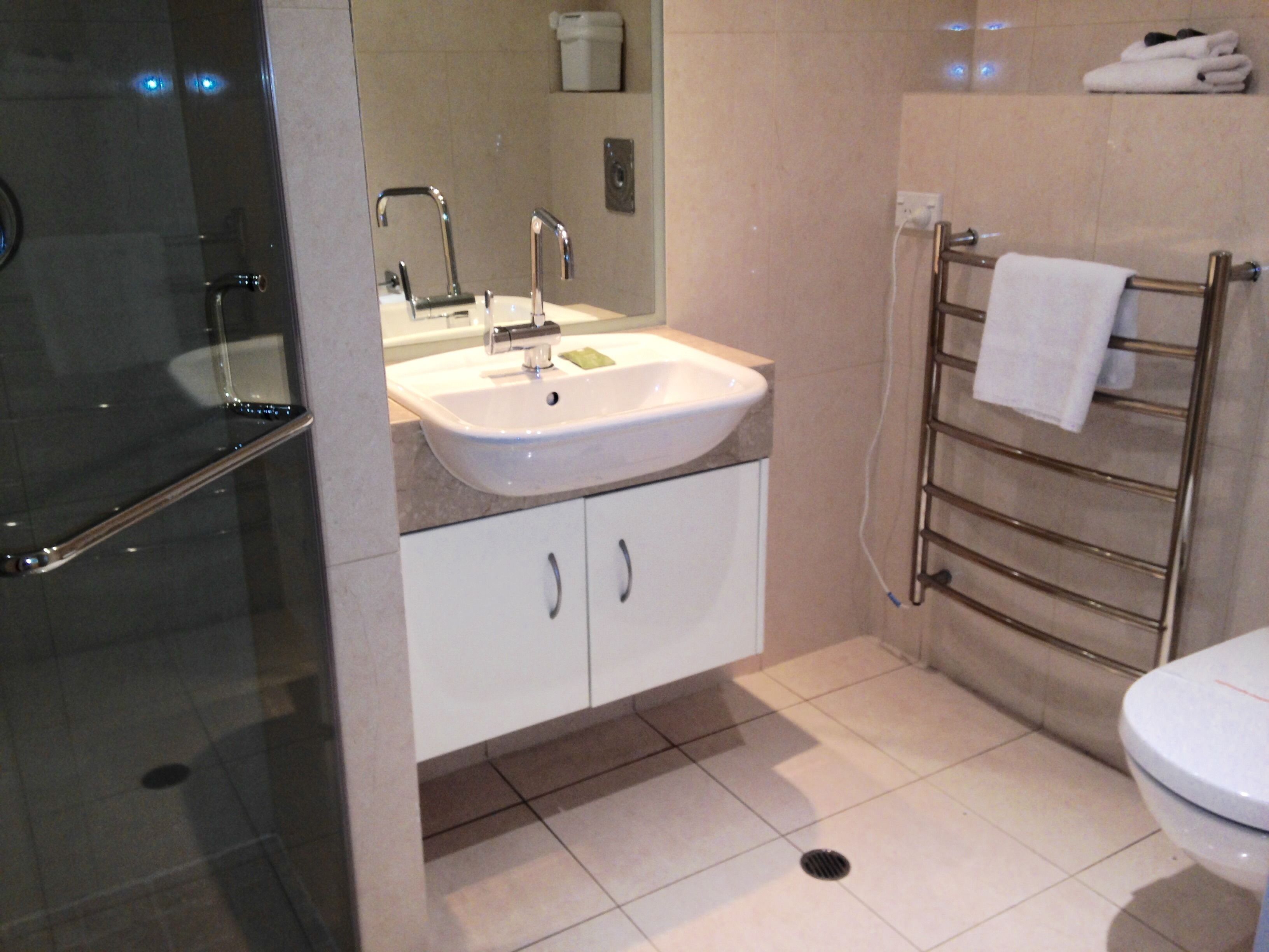 Une salle de bain moderne avec une douche à parois de verre, un lavabo blanc avec un miroir, un porte-serviettes et des toilettes.