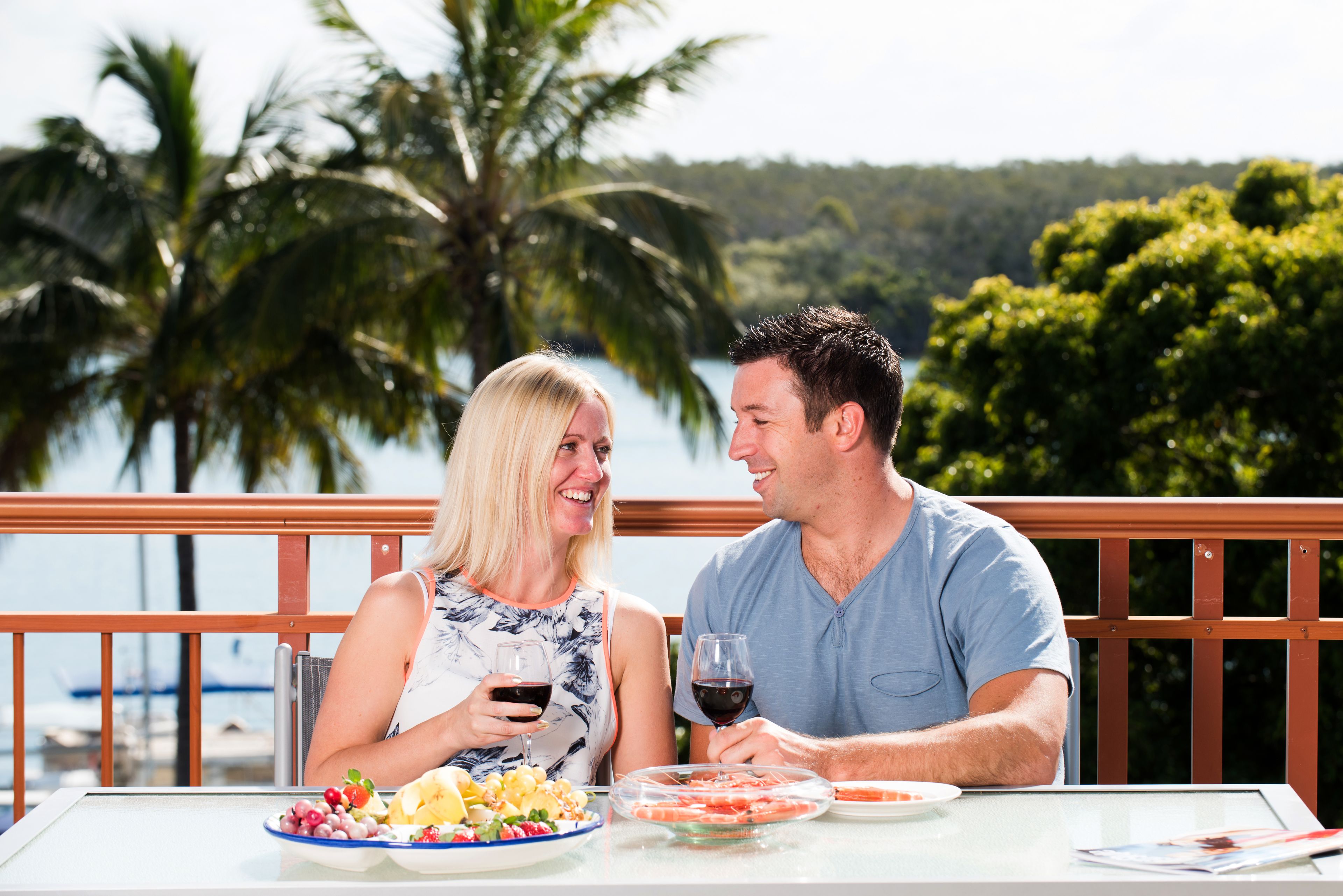Um casal jantando à mesa com vista para um lago e palmeiras.