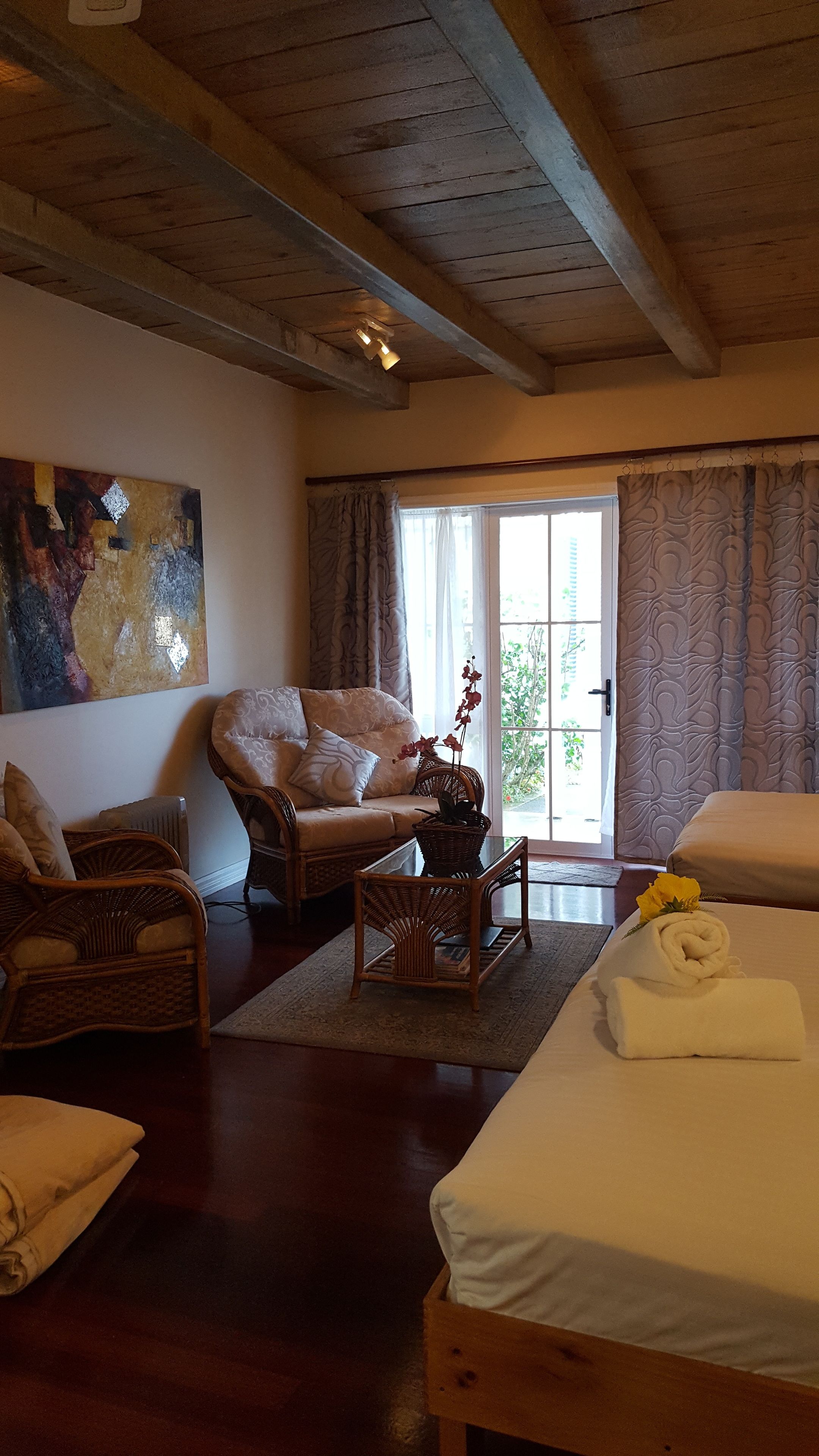 A cozy room with a bed, a wicker chair, a table with a plant, and a painting on the wall.