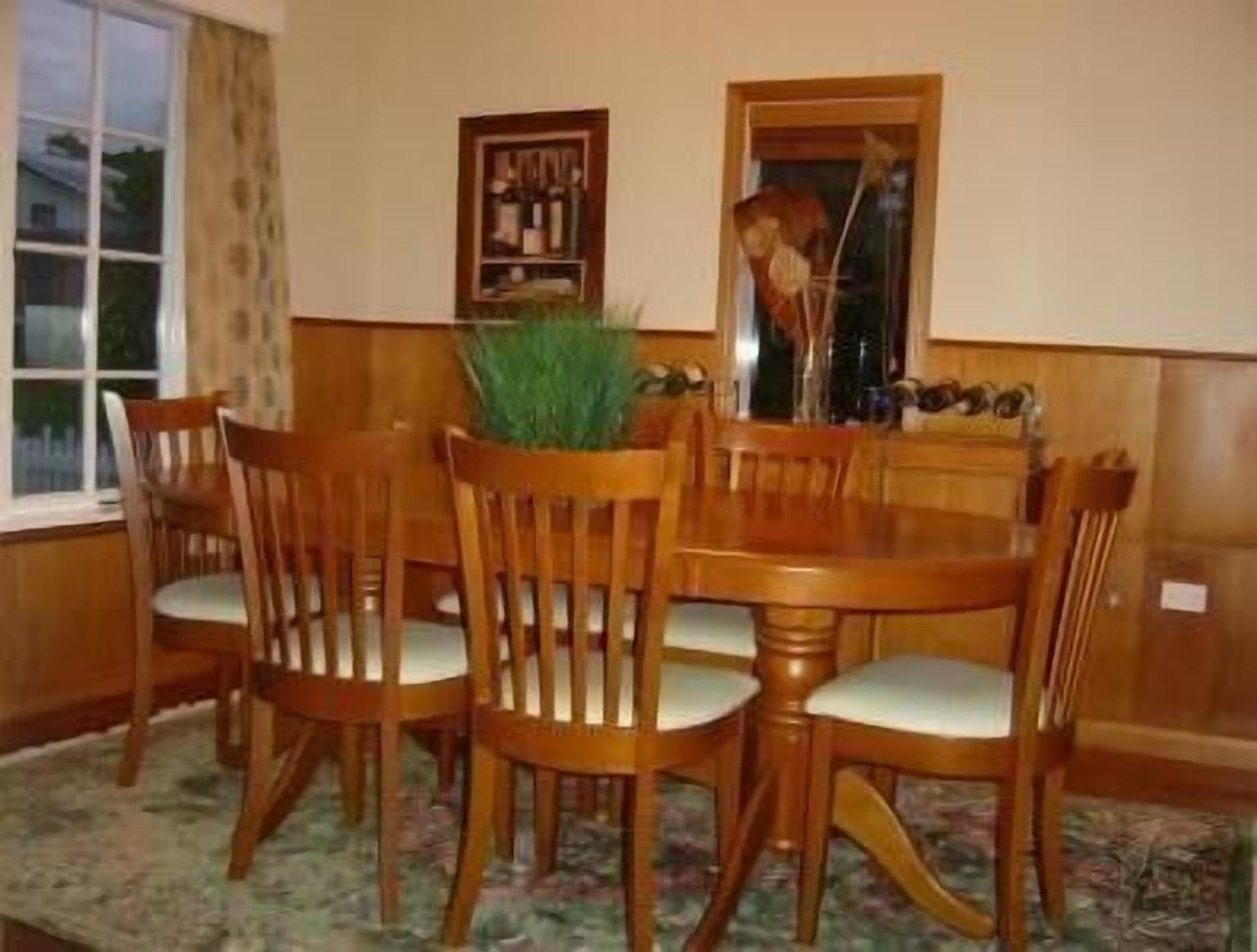 Un coin repas avec une table ronde en bois et six chaises, une petite plante en pot et une fenêtre avec des rideaux.