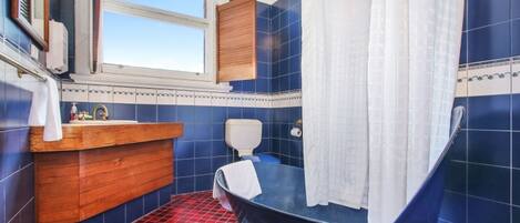 Un baño con bañera, tocador de madera, inodoro y ventana.