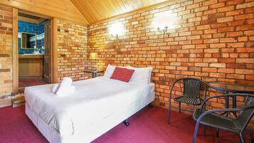 Une pièce avec un mur en briques, un lit avec une literie blanche, un oreiller rouge et deux chaises.