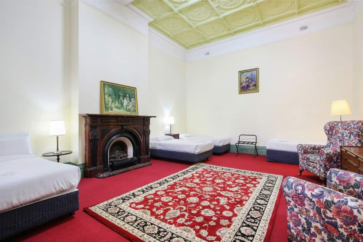 A hotel room with a large bed, a smaller bed, a fireplace, a red carpet, and a floral armchair.