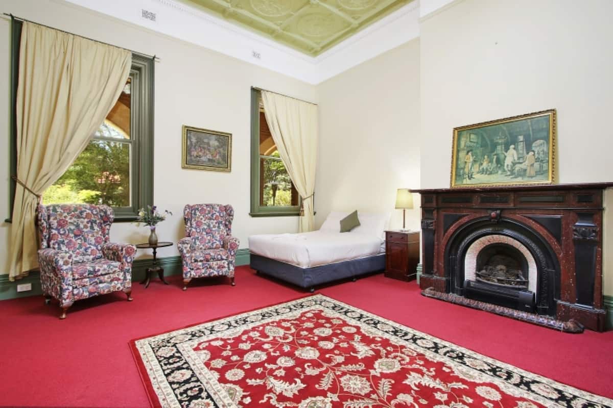 A room with a bed, two armchairs, a fireplace, and a large rug.