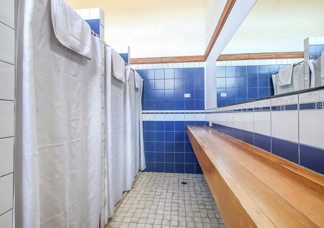 Un baño con paredes de azulejos azules y blancos, una banca de madera y una cortina blanca.