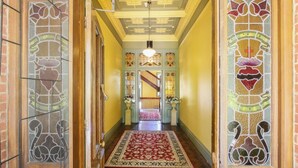 A hallway with a patterned carpet, wooden doors with stained glass, and a staircase with a red carpet. - The Priory Beechworth (Beechworth)