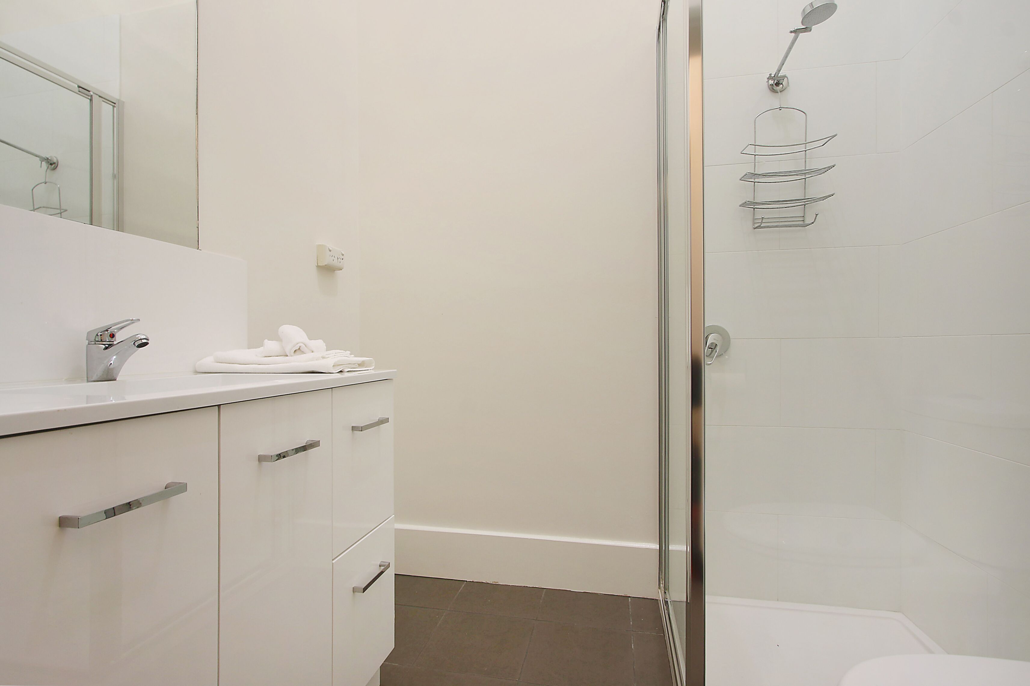 Un baño moderno con cabina de ducha de vidrio, un lavamanos blanco con una toalla y un espejo.