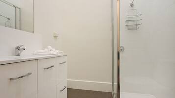 Un baño moderno con cabina de ducha de vidrio, un lavamanos blanco con una toalla y un espejo.