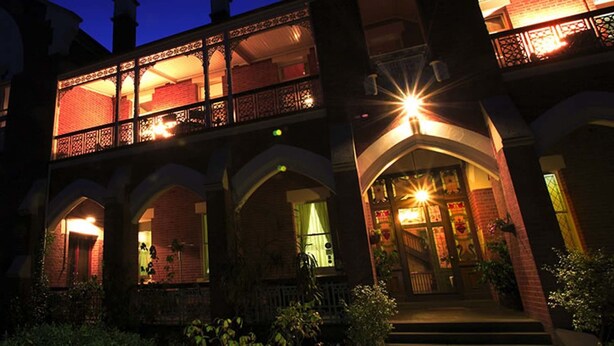 A multi-story building with a balcony, arched windows, and a well-lit entrance. - The Priory Beechworth (Beechworth)