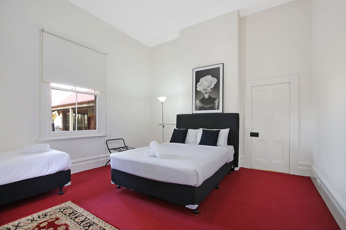 A hotel room with two beds, a red carpet, a white wall, a framed picture, and a window with a view.