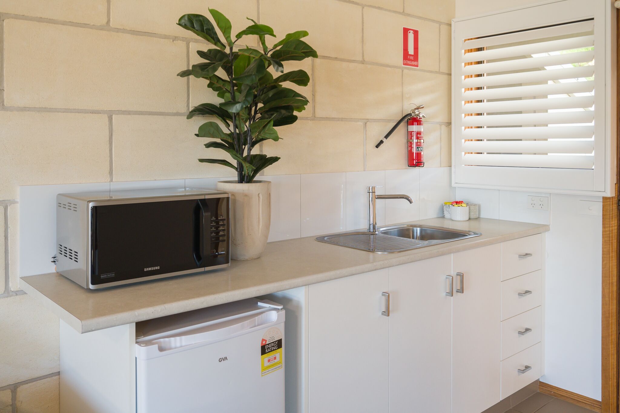 Una cocina compacta con microondas, lavabo y un refrigerador pequeño.