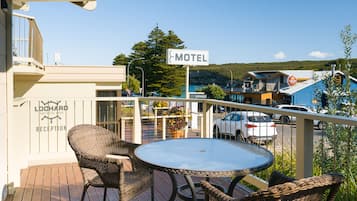 A motel with a reception area, a balcony with wicker furniture, and a view of the surrounding area including a car and a building with a 'Motel' sign.