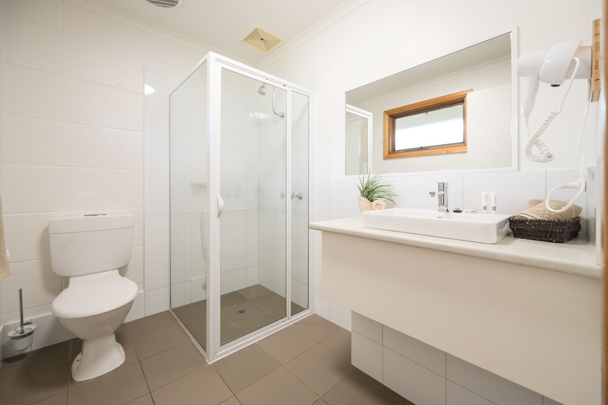 Une salle de bain moderne équipée de toilettes, d’une douche à parois de verre, d’un lavabo avec un miroir au-dessus et d’un sèche-cheveux fixé au mur.