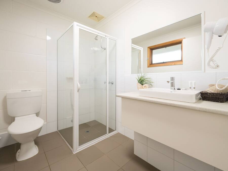 A modern bathroom with a toilet, a glass-enclosed shower, a sink with a mirror above, and a hairdryer on the wall.