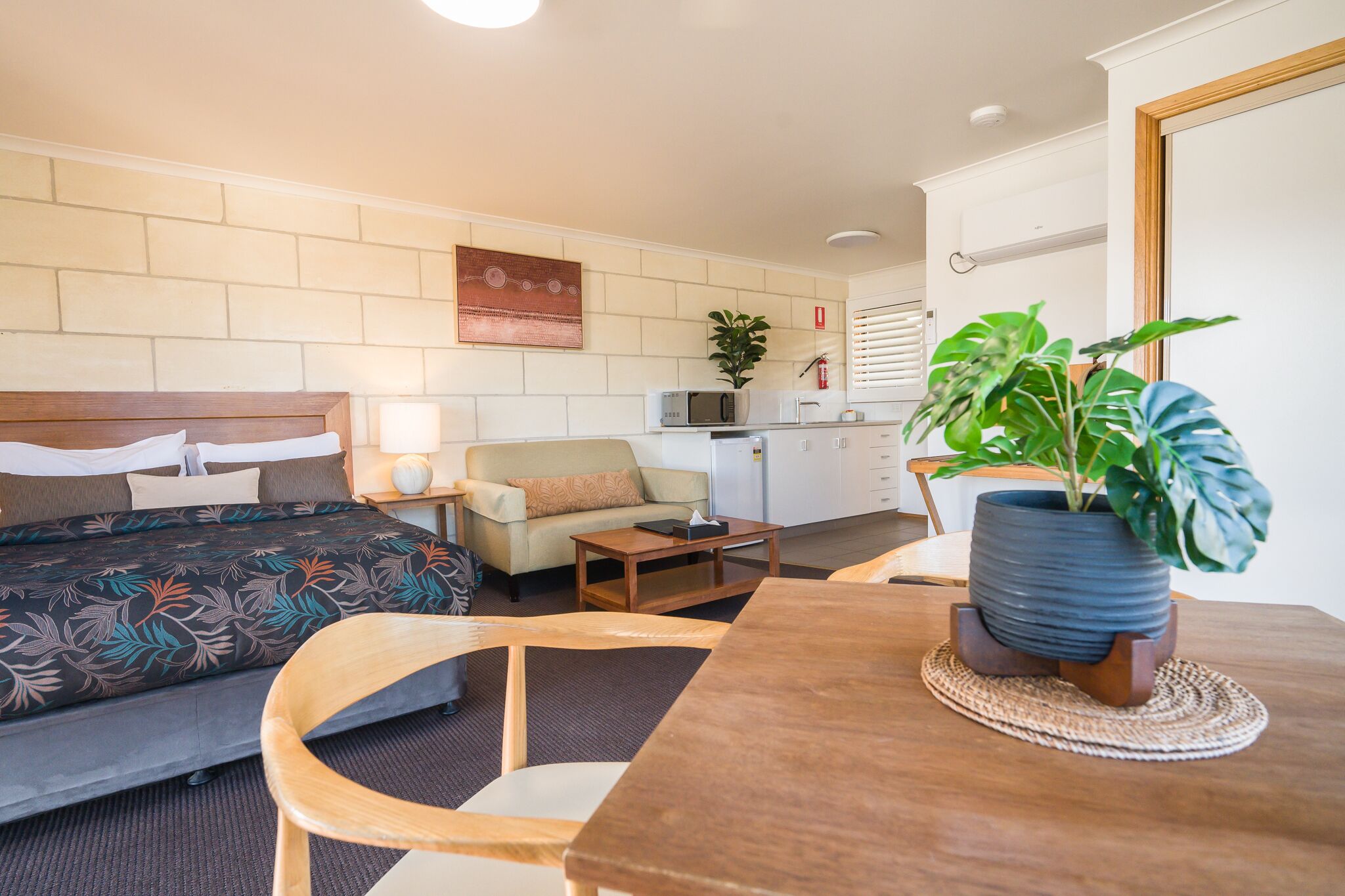 A hotel room with a bed, a sofa, a dining table, and a potted plant.