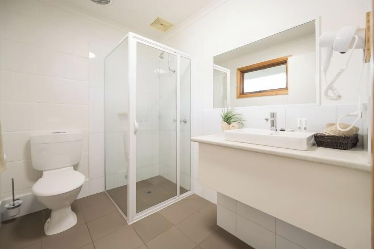 A modern bathroom with a toilet, a glass-enclosed shower, a sink with a mirror, and a hairdryer mounted on the wall.