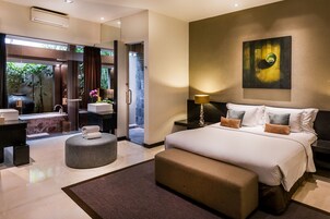 Une chambre d’hôtel moderne dotée d’un grand lit, d’un coin salon, d’une salle de bain avec baignoire et offrant une vue sur la verdure.