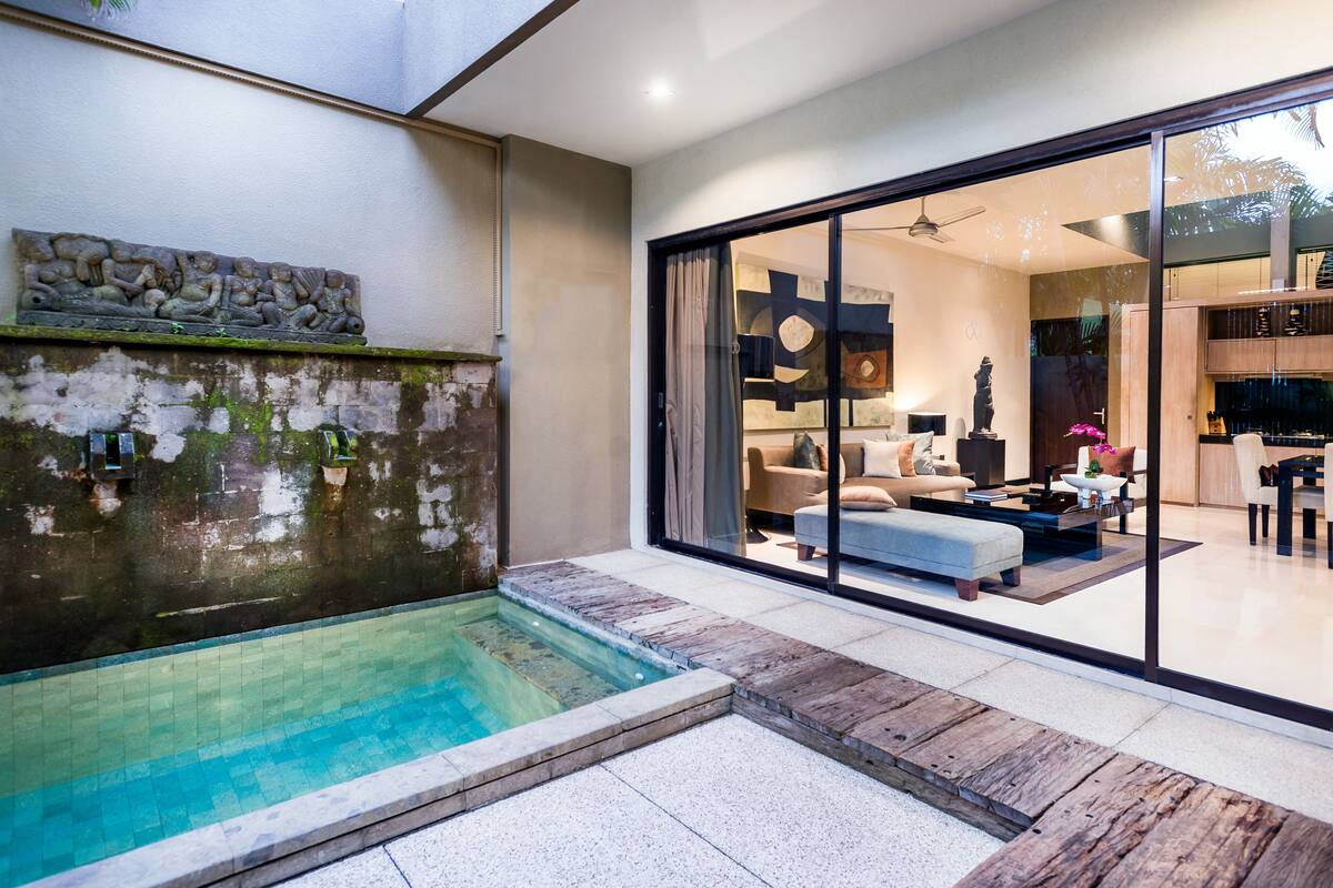 A modern indoor pool area with a stone wall and a glass door leading to a living room.